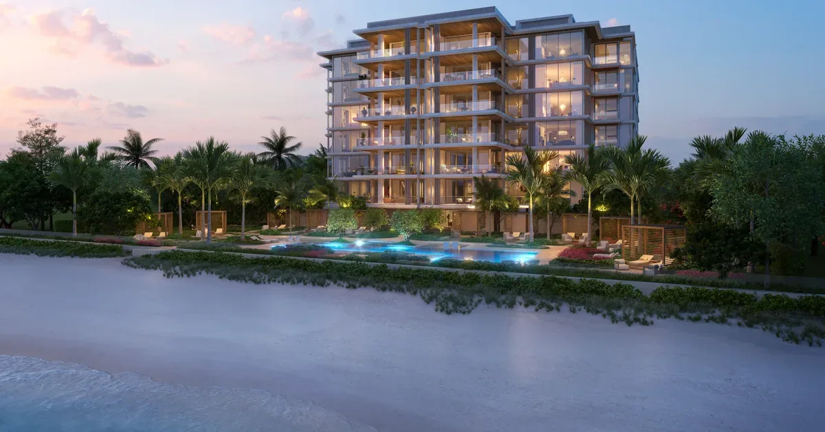 Luxury beachfront condominium tower glows at dusk with illuminated pool terrace, palm trees, and direct oceanfront access on a pristine sandy shore.